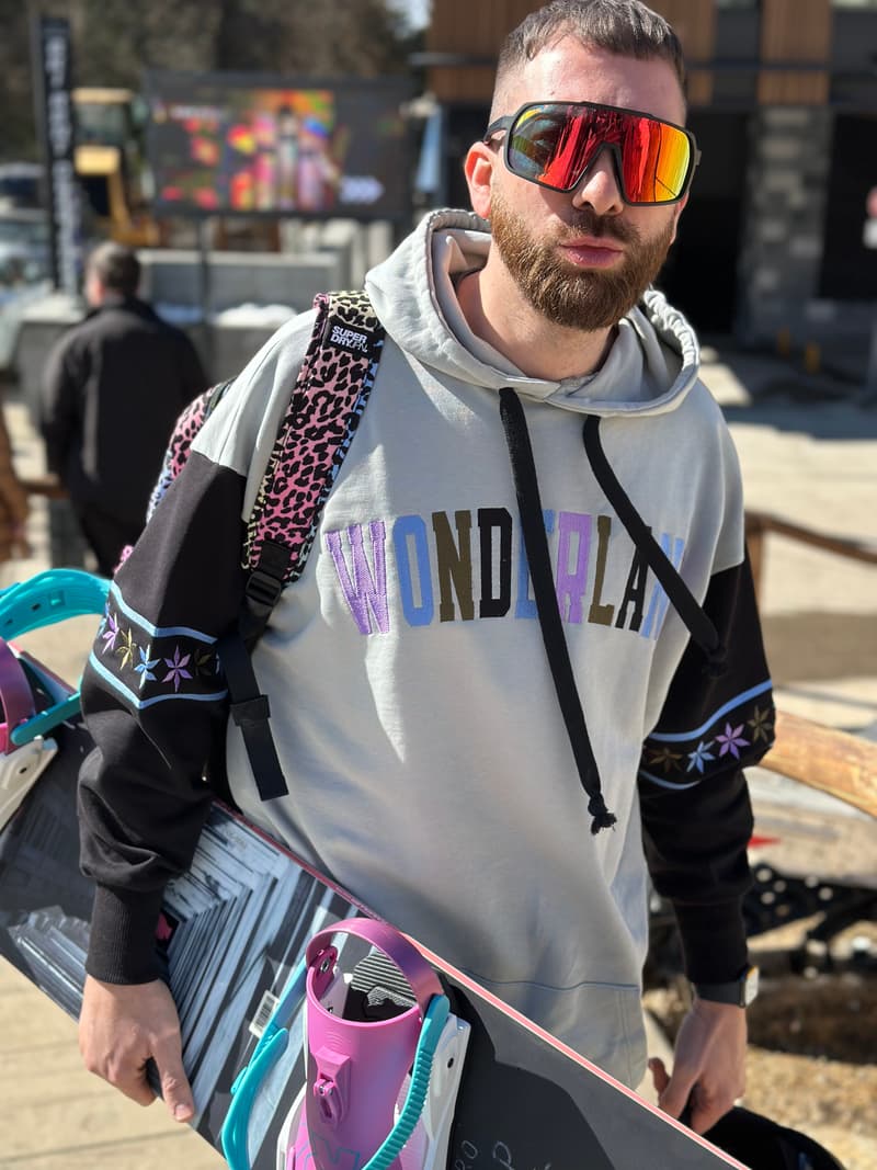 Muškarac u šarenoj varijanti Wonderland duksa LONG, krupan kadar sa snowboardom